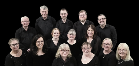 A group of fourteen members of the Cantiunculae choir wearing black tops in front of a black background
