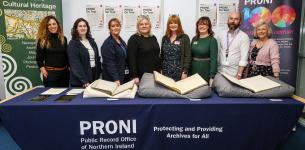 Group of eight men and women standing behind a large table with documents and books on display.