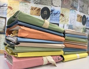Side-view of two stacks of files, all of varying colours on a table.