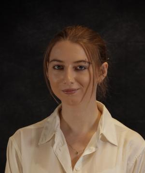 Headshot of a young woman with red hair in a white shirt over a black background.