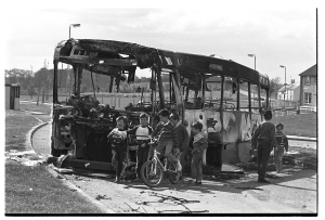 Black and white photograph of a group of seven young children playing around the remains of a burned bus