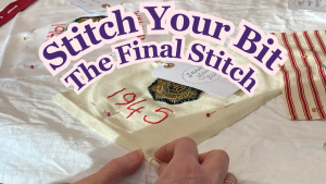 A hand is stitching a piece of white fabric with '1945' embroidered on it, on to a larger piece of white fabric.