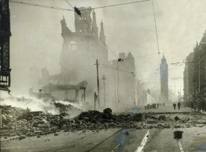 Black and white photograph of a destroyed Belfast street with rubble on the ground - The outline of the Albert Clock can be seen in the distance