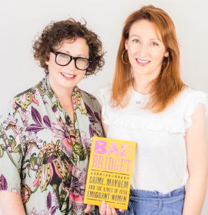 Two women stand side-by-side holding up the book they have written, 'Bad Bridget'. One woman wears glasses and has short curly hair, the other woman has long red hair.