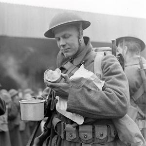 black and white photograph of an American soldier during the Second World War eating a pie and holding a tin cup 