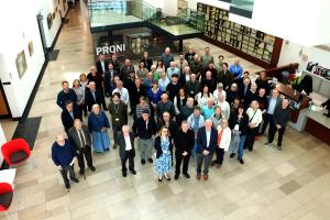 A large group of around 50 people stand in the PRONI atrium
