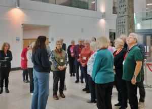 A woman with brown hair speaking to a group of people in the PRONI foyer