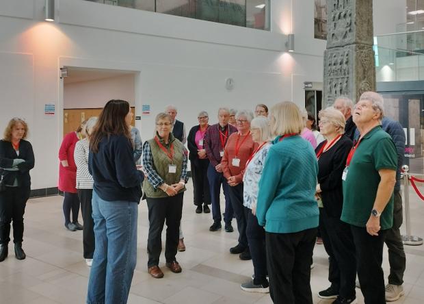 Group of people wearing lanyards standing in the PRONI foyer listening to a PRONI staff member lead a tour