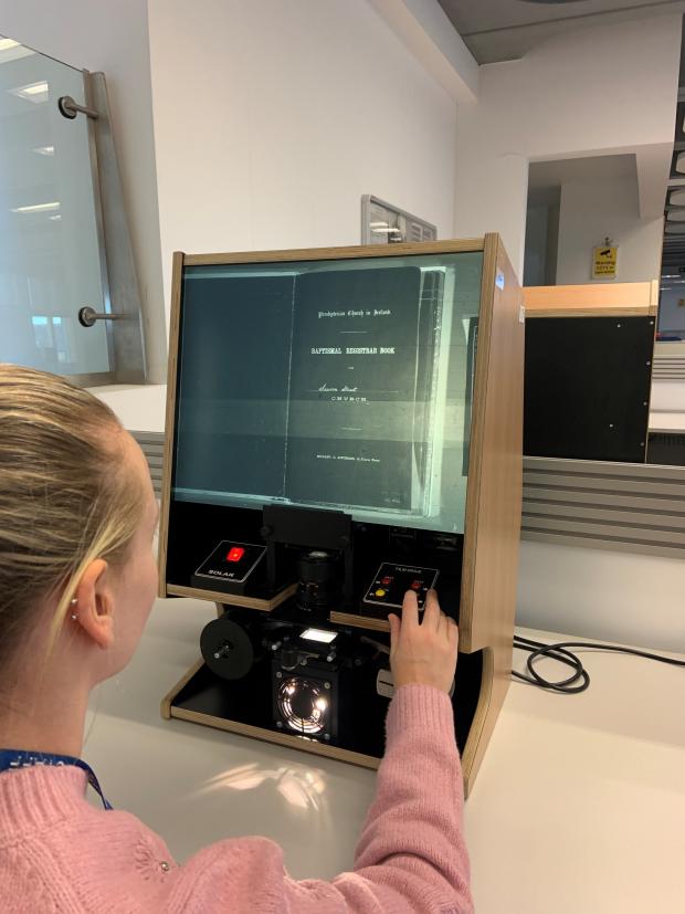 Woman looking at an image on a microfilm reader on a large table.