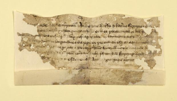 Small piece of an archival document with writing on the front and visible damage around the edges. The piece has been attached to yellow archival paper.