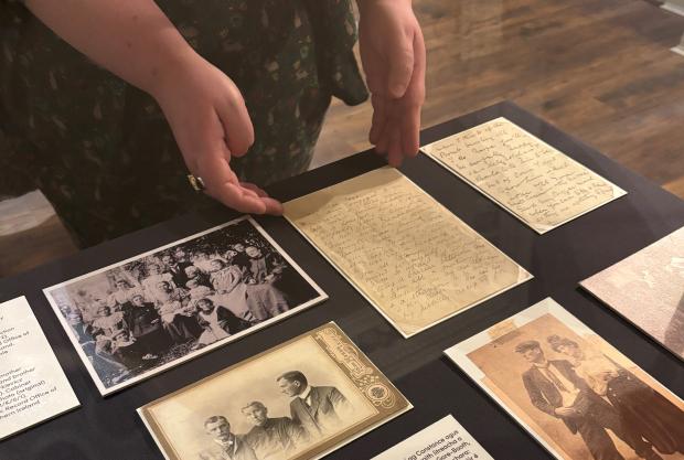 Table with around 7 archival photographs and letters on display. A pair of hands is visible steadying one of the items.