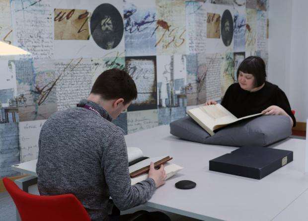Man and woman sitting across from each other reading volumes on a large table.