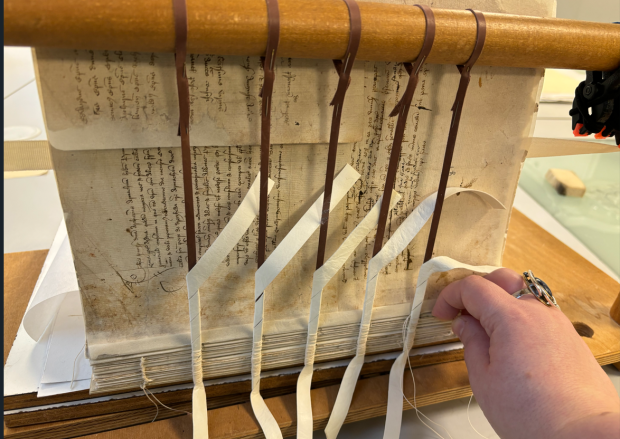Archival book with no binding attached to a large wooden device for treatment.