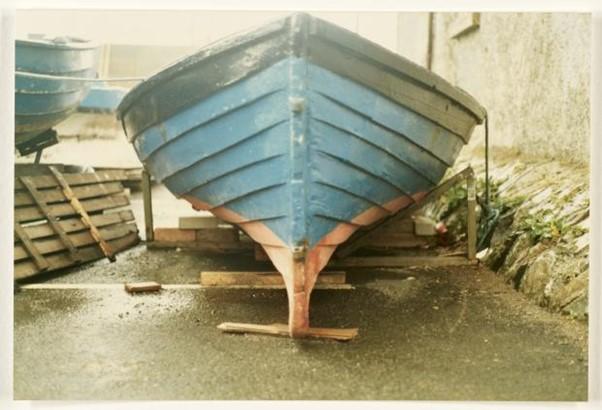 Old front-view photograph of a blue boat with a black trim on land.