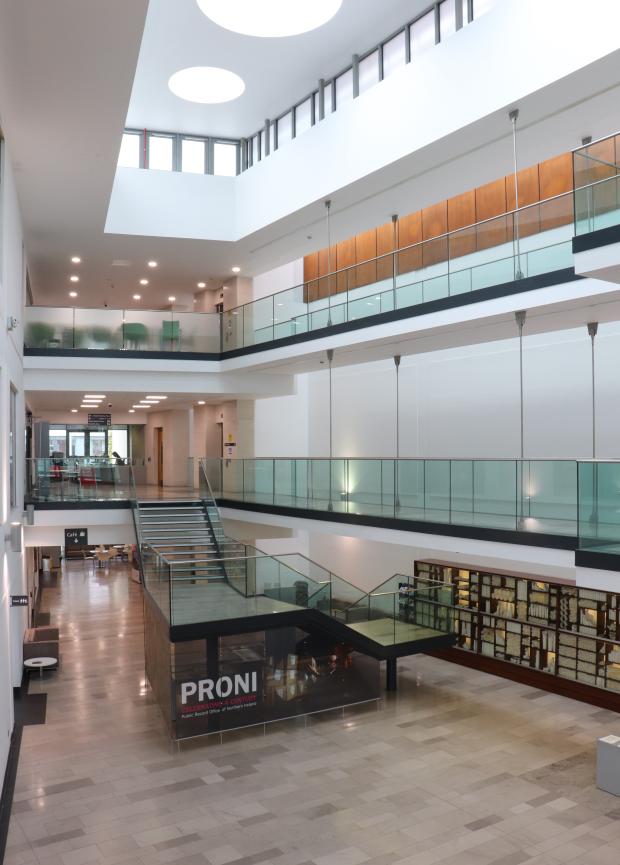 Image of the interior of a large building with three floors and windows on the ceiling. A central staircase with the PRONI logo is visible between the ground and first floor.