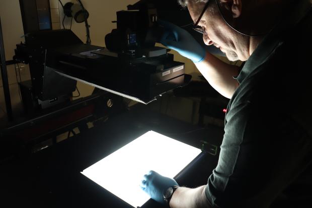 Man with latex gloves standing behind large equipment that shines a bright light onto a surface.