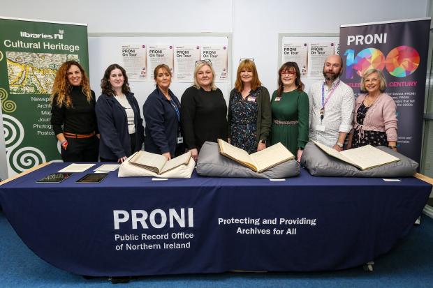 Group of eight men and women standing behind a large table with documents and books on display.