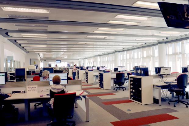 Image of a large room with windows along the length of the right hand side and two rows of desks with multiple computers at each.