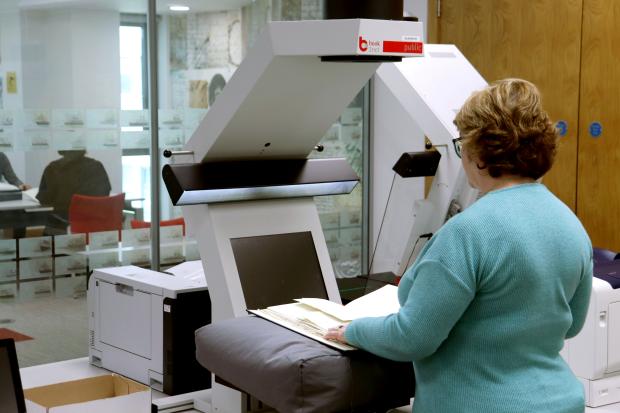 Woman in a blue top with a book on a large cushion under a large white machine.