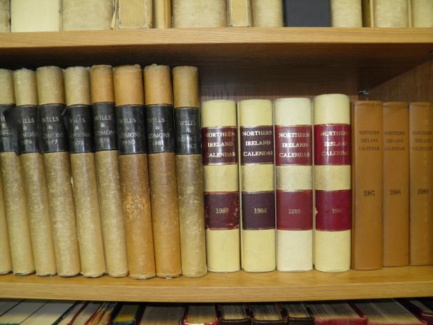 15 books ranging in size on a shelf that read either "wills & admons" or "Northern Ireland Calendar" followed by a year on the spine.