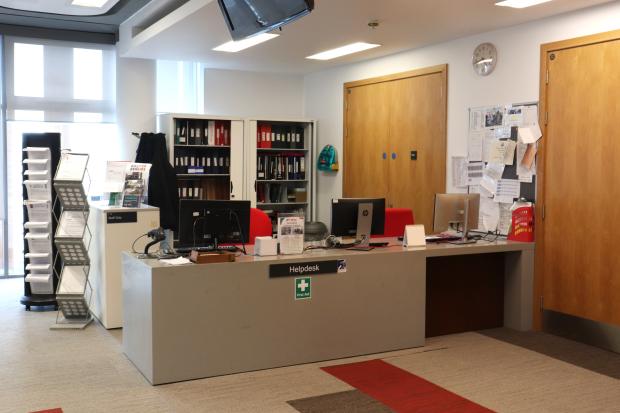 Image of a large reception desk in an office room, with visible file shelves behind and two computers visible.